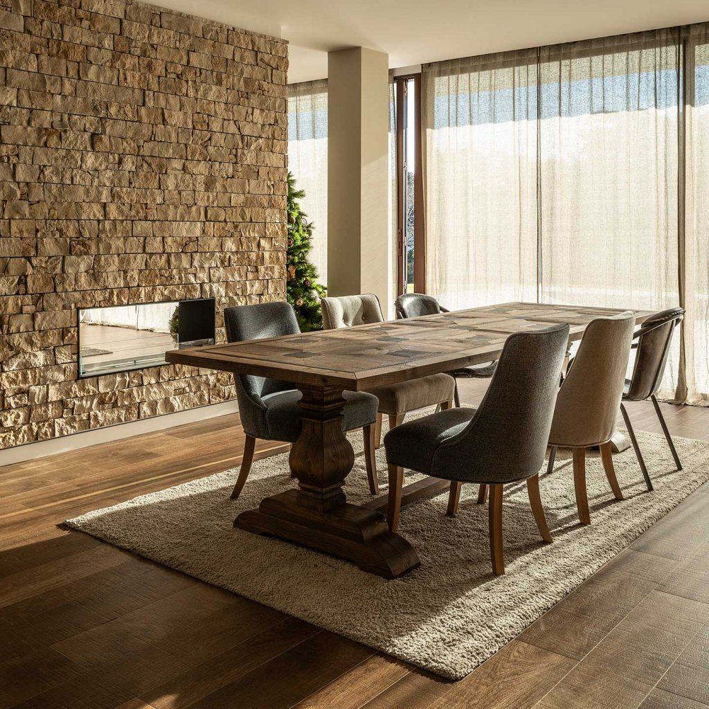 Elegant dining room featuring a textured STONEPANEL™ wall, a rustic wooden table, and upholstered chairs, bathed in warm natural light.