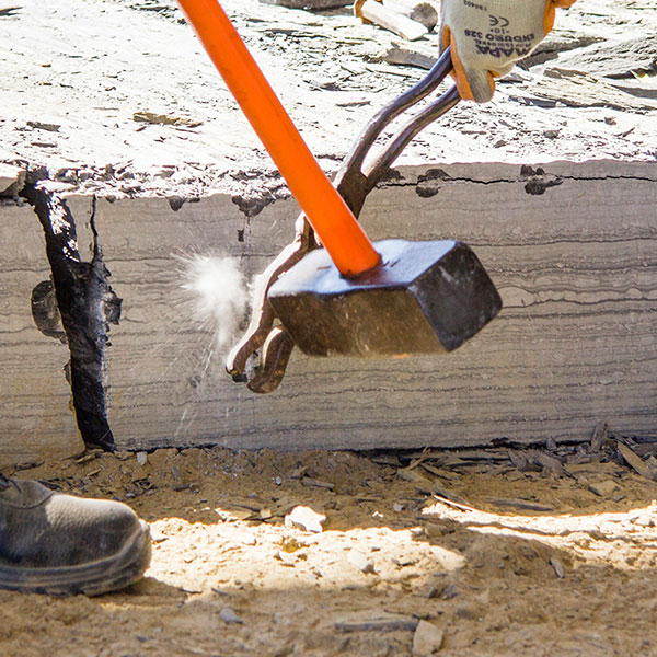 Worker shaping a block of Infercoa schist in the quarry using traditional tools.