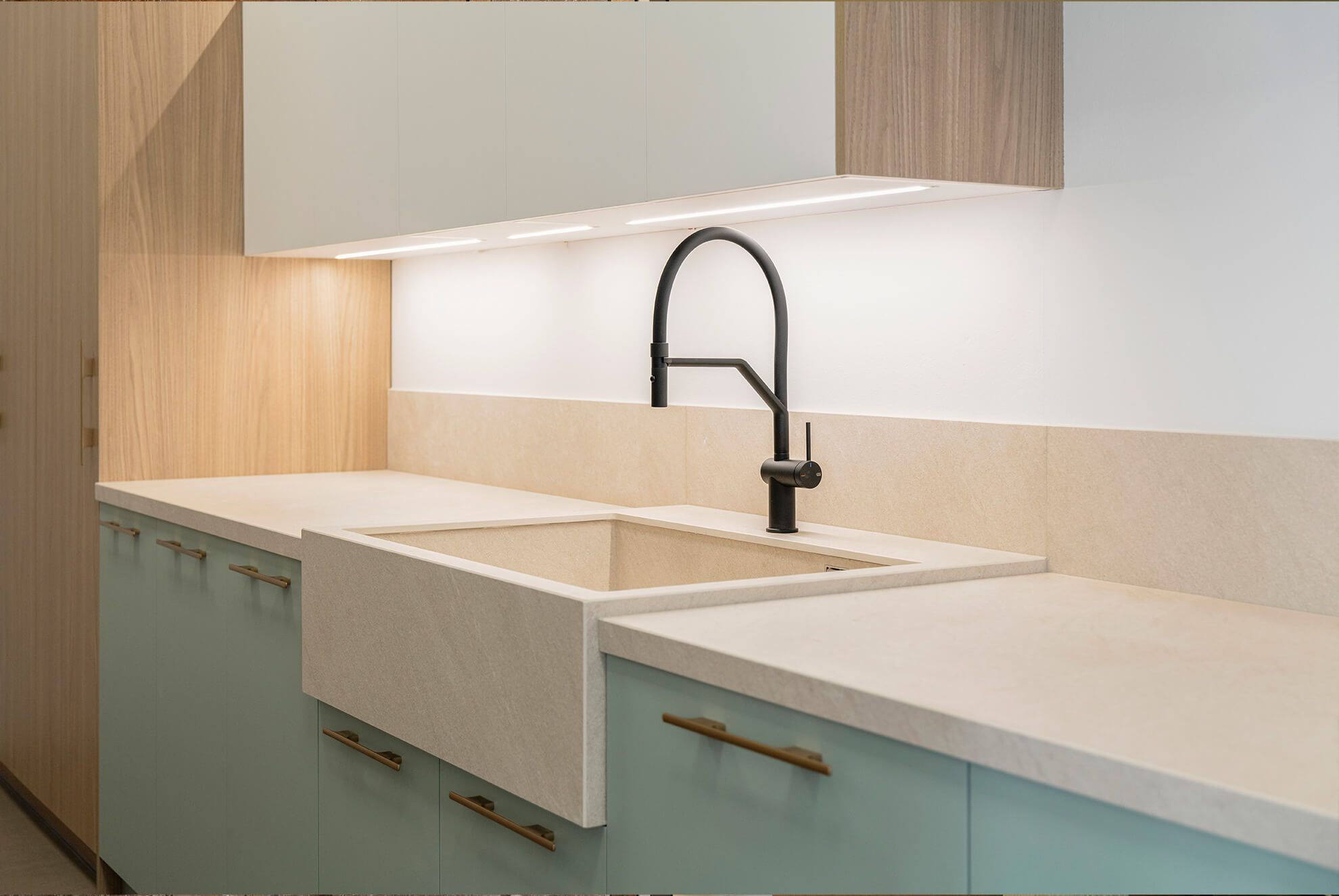 Modern kitchen with a Ceratop® Duna porcelain countertop and sink, featuring soft beige tones, pastel green cabinetry, and a sleek black faucet.