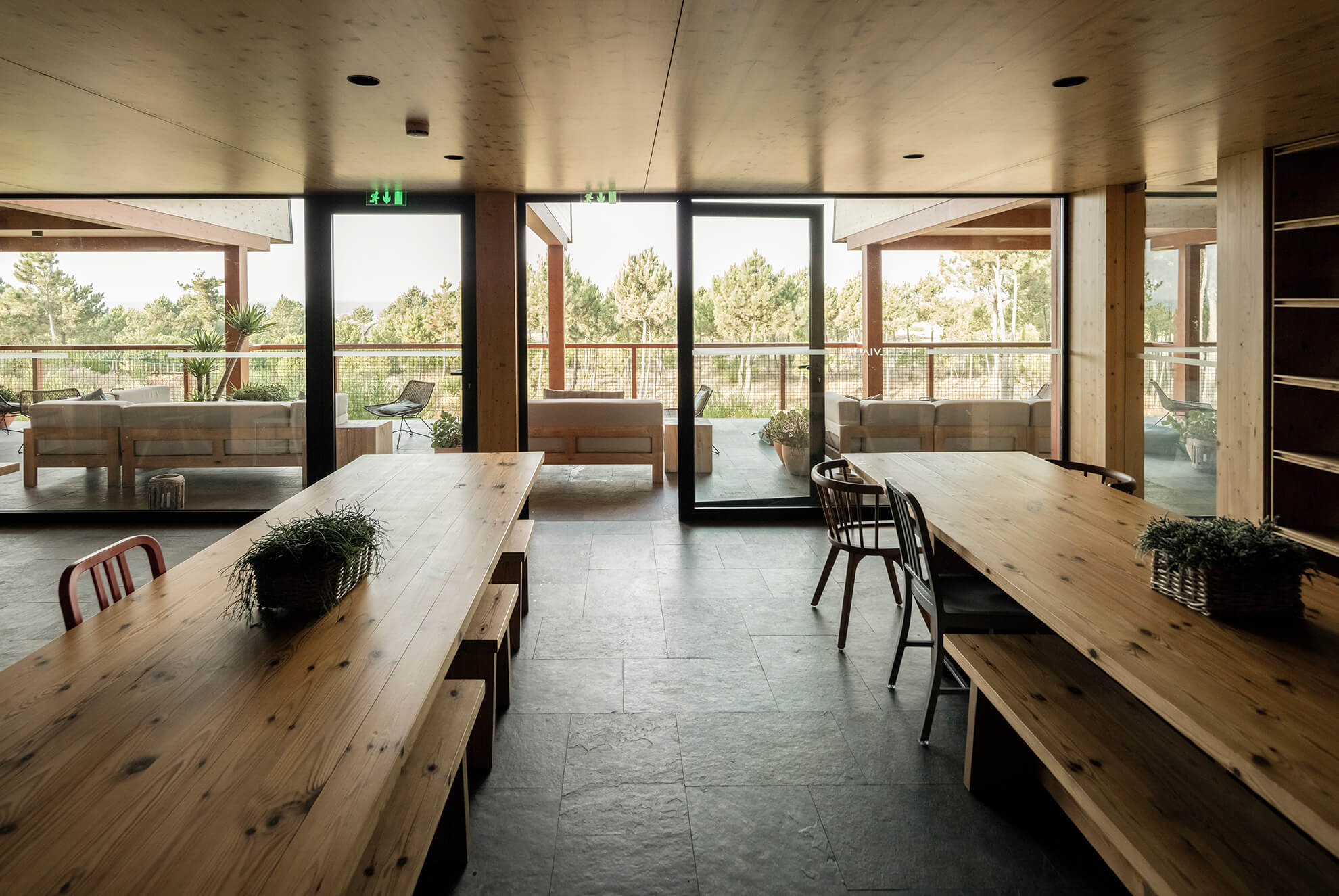 Spacious dining and lounge area with Brazilian multicolor slate flooring, wooden tables, and large glass doors leading to an outdoor terrace.