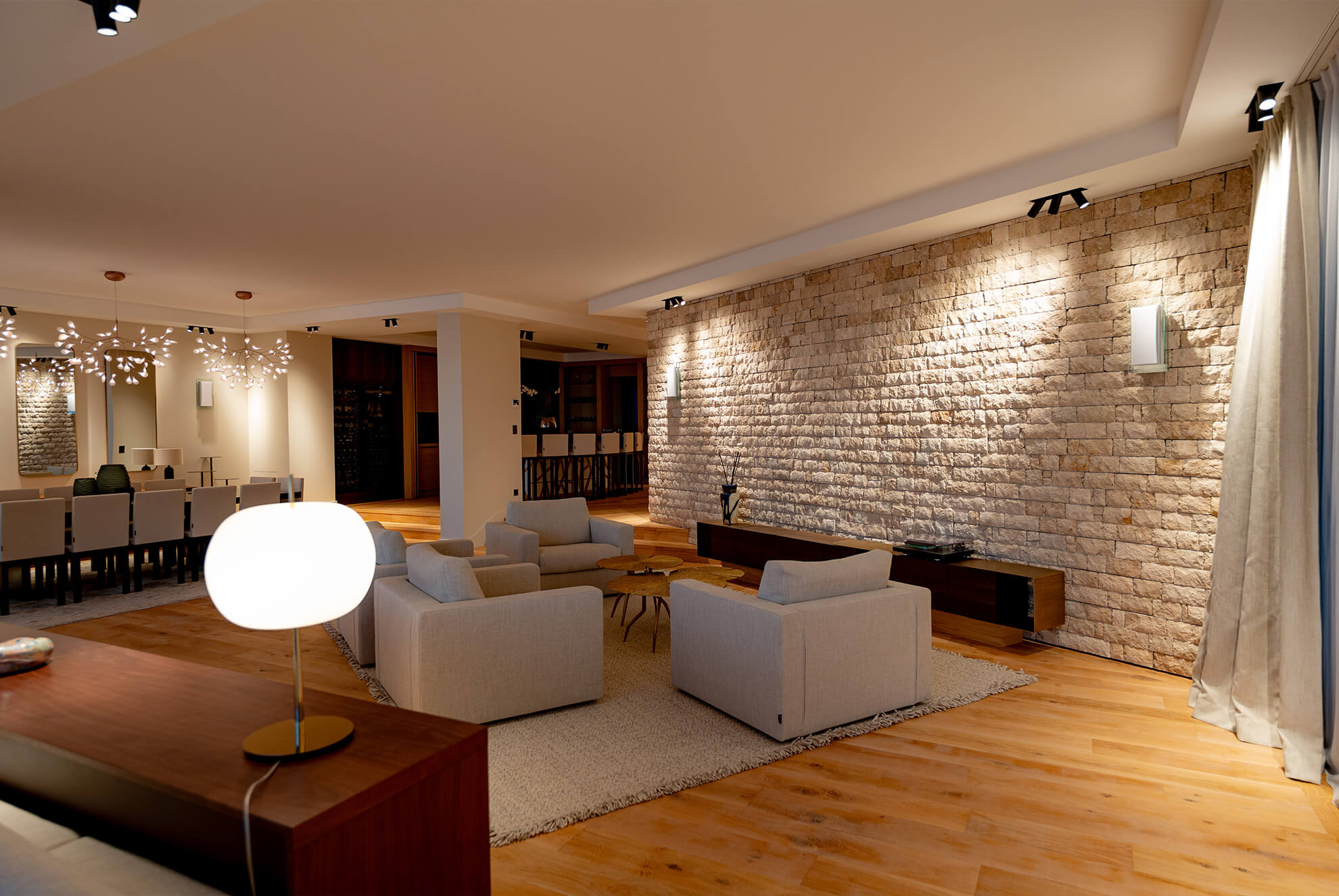 Elegant living and dining area with a STONEPANEL™ Sabbia natural stone feature wall, warm wooden flooring, and modern lighting.