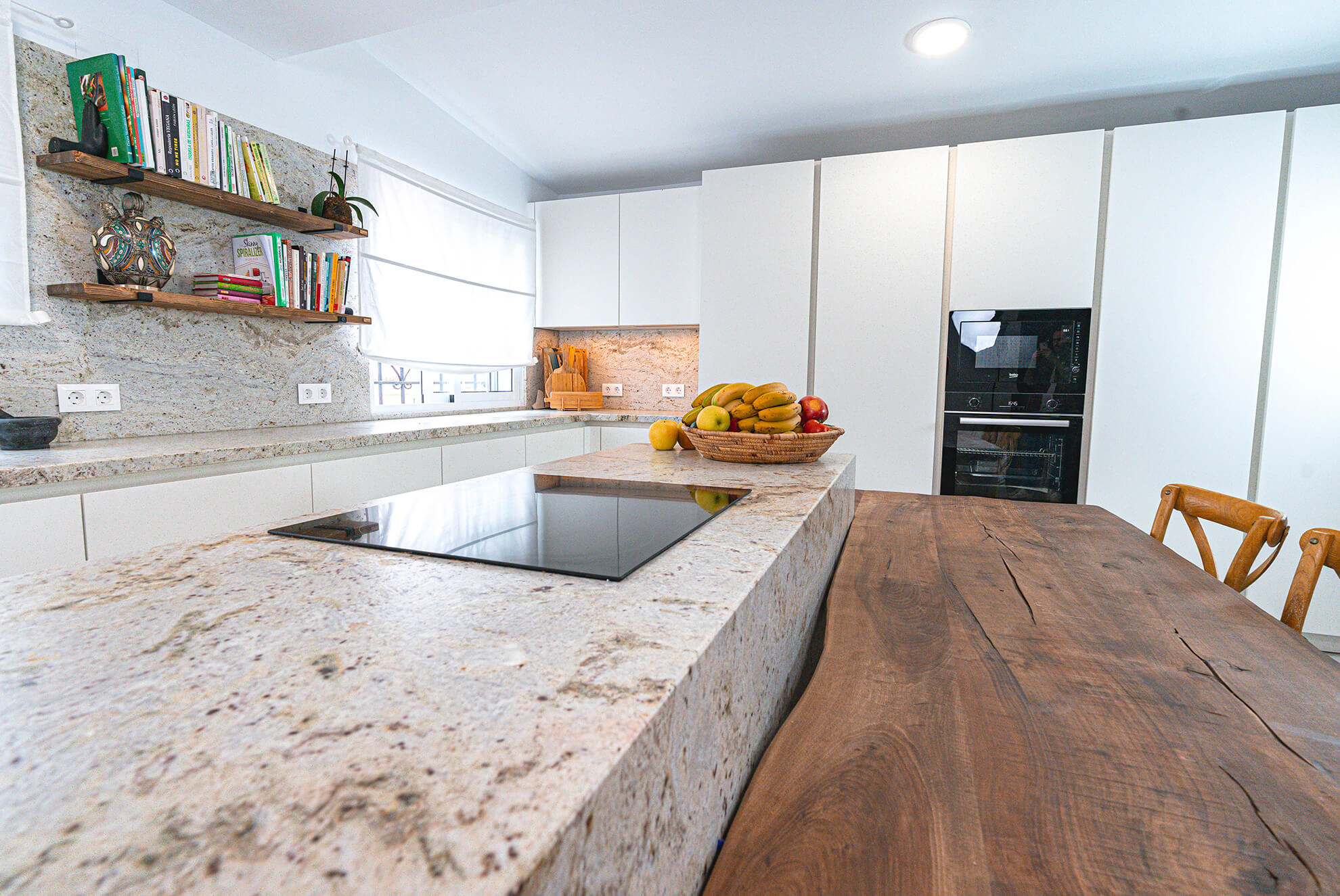 Modern kitchen with a Persia Bianca granite countertop, a wooden dining table, white cabinetry, and open shelving with books and decorative elements.